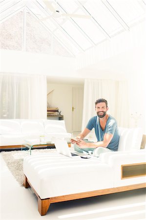 Man using laptop on sofa in modern living room Stock Photo - Premium Royalty-Free, Code: 6113-07790570