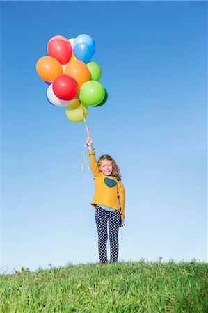 Girl holding bunch of balloons on grassy hill Stock Photo - Premium Royalty-Free, Code: 6113-07731261