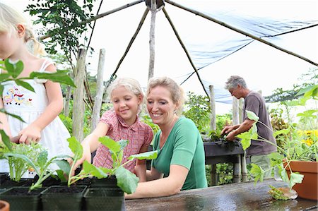 Smiling woman with two girls looking at seedlings in greenhouse, man in background Stock Photo - Premium Royalty-Free, Code: 6113-07808438