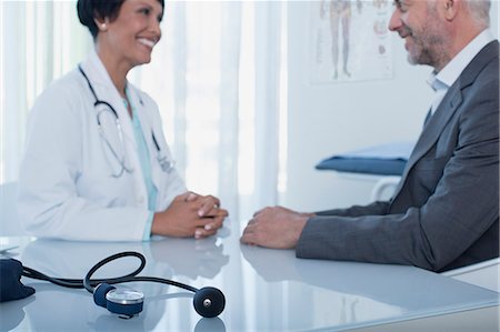 doctor patient consultation - Smiling female doctor talking to patient at desk in office, blood pressure gauge in foreground Stock Photo - Premium Royalty-Free, Code: 6113-07808666