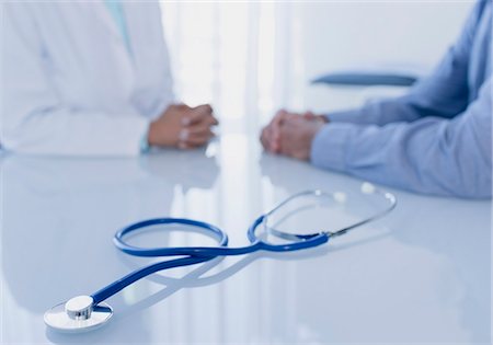 Stethoscope on white desk in doctor's office, female doctor and patient sitting in background Stock Photo - Premium Royalty-Free, Code: 6113-07808675