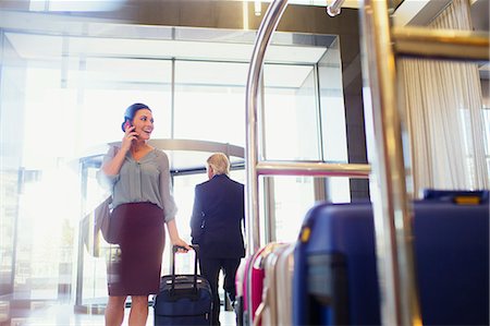 Smiling woman talking on phone in hotel lobby, luggage cart in foreground Stock Photo - Premium Royalty-Free, Code: 6113-07808626