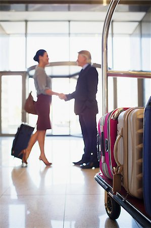 Man and woman shaking hands in hotel lobby, luggage cart in foreground Stock Photo - Premium Royalty-Free, Code: 6113-07808635