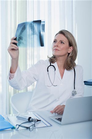 simsearch:614-06813654,k - Female doctor looking at x-ray at desk with laptop in office Foto de stock - Sin royalties Premium, Código: 6113-07808702