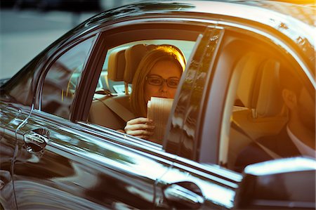Businesswoman reading newspaper in back seat of car Stock Photo - Premium Royalty-Free, Code: 6113-07961607