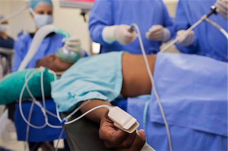 surgical gown - Doctors performing laparoscopic surgery, patient with pulse oxymeter on finger Photographie de stock - Premium Libres de Droits, Code: 6113-07905942