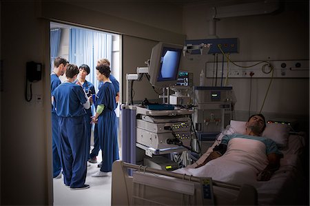 Patient lying in bed in intensive care unit, team of doctors discussing in background Foto de stock - Sin royalties Premium, Código: 6113-07905962