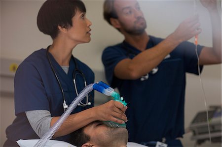 Doctor holding oxygen mask over patient, doctor adjusting IV drip in intensive care unit Stock Photo - Premium Royalty-Free, Code: 6113-07905917