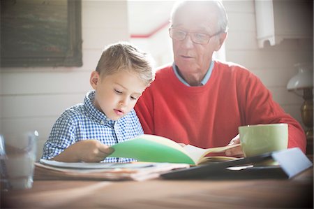 Boy reading with grandfather at table Foto de stock - Sin royalties Premium, Código: 6113-07906344
