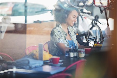 Smiling woman with headphones at laptop in cafe Stock Photo - Premium Royalty-Free, Code: 6113-08171258