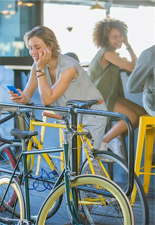 simsearch:6113-07543477,k - Smiling woman leaning on railing texting with cell phone above bicycle Stock Photo - Premium Royalty-Free, Code: 6113-08171272