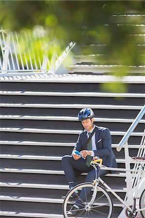 Businessman with helmet and bicycle texting with cell phone on urban stairs Stock Photo - Premium Royalty-Free, Code: 6113-08171279