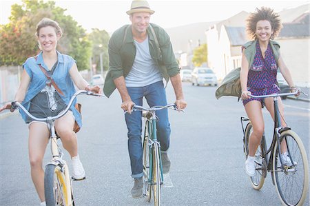 simsearch:6113-08321095,k - Smiling friends riding bicycles on street Stock Photo - Premium Royalty-Free, Code: 6113-08171300