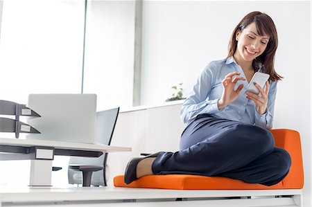 simsearch:6113-06908958,k - Smiling businesswoman texting with cell phone on cushion in office Foto de stock - Sin royalties Premium, Código: 6113-08171427