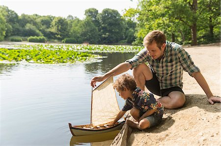 Father and son playing with toy sailboat at lakeside Photographie de stock - Premium Libres de Droits, Code: 6113-08220225