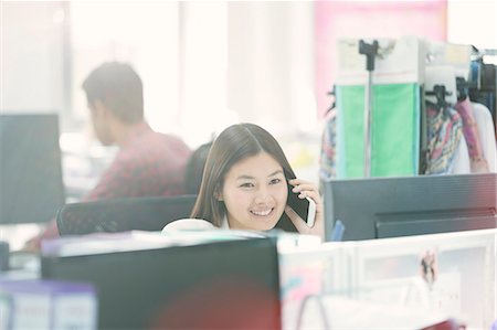 face to internet technology - Smiling fashion designer talking on cell phone at desk in office Photographie de stock - Premium Libres de Droits, Code: 6113-08220331