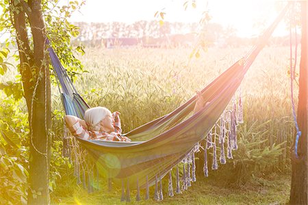 relaxar - Serene woman napping in hammock next to sunny rural wheat field Foto de stock - Royalty Free Premium, Número: 6113-08220463
