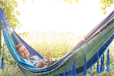 Carefree boy listening to music on mp3 player in rural hammock Stock Photo - Premium Royalty-Free, Code: 6113-08220498