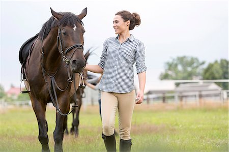 Smiling woman walking horse in rural pasture Stock Photo - Premium Royalty-Free, Code: 6113-08220421
