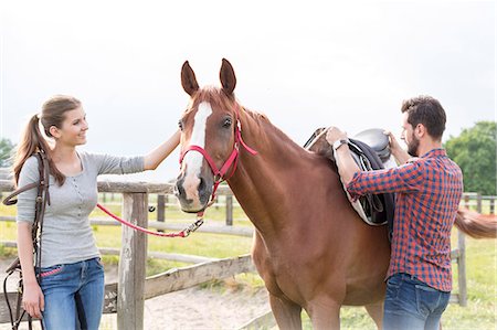 Couple saddling horse in rural pasture Stock Photo - Premium Royalty-Free, Code: 6113-08220437