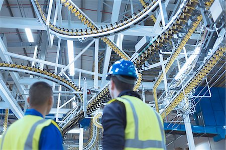 Workers looking up at winding printing press conveyor belts overhead Stock Photo - Premium Royalty-Free, Code: 6113-08393626