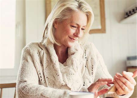 photo mature - Smiling senior woman in sweater texting with cell phone in kitchen Stock Photo - Premium Royalty-Free, Code: 6113-08393731