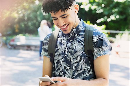 student texting on cell phone - Smiling man with curly black hair listening to music with headphones and mp3 player Stock Photo - Premium Royalty-Free, Code: 6113-08321193