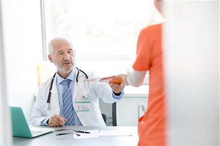 Doctor at desk giving medical record to nurse in doctor's office Stock Photo - Premium Royalty-Free, Code: 6113-08321285