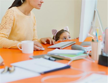 Girl in mouse ears headband watching mother work at computer Stock Photo - Premium Royalty-Free, Code: 6113-08321634