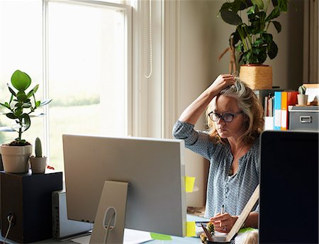 Stressed woman with hand in hair holding credit card at computer in home office Stock Photo - Premium Royalty-Free, Code: 6113-08321788