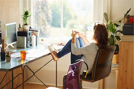 Pensive woman looking through window with feet up on desk in sunny home office Stock Photo - Premium Royalty-Free, Code: 6113-08321812