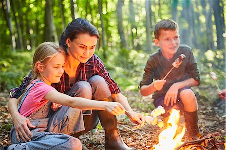 Family roasting marshmallows at campfire in forest Stock Photo - Premium Royalty-Free, Code: 6113-08424174
