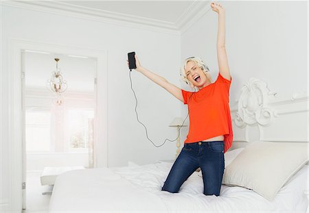 simsearch:649-06532718,k - Playful women kneeling on bed listening to music with mp3 player and headphones Stock Photo - Premium Royalty-Free, Code: 6113-08550048