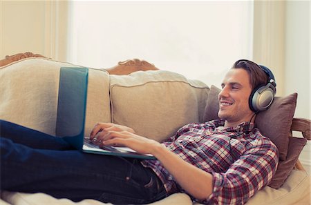 simsearch:6113-07731119,k - Man with headphones using laptop on living room sofa Stock Photo - Premium Royalty-Free, Code: 6113-08550097