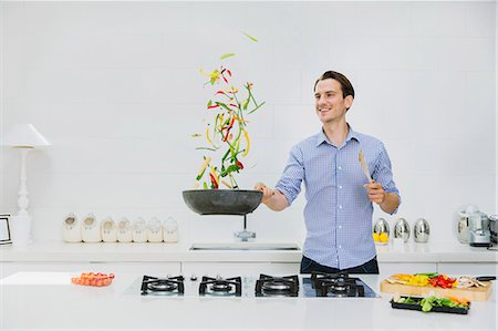 sauteeing - Smiling man flipping vegetables in skillet in kitchen Photographie de stock - Premium Libres de Droits, Code: 6113-08550029