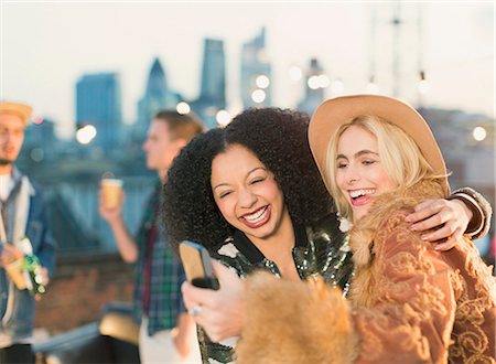 simsearch:6113-07146985,k - Laughing young women taking selfie at rooftop party Foto de stock - Sin royalties Premium, Código: 6113-08568584