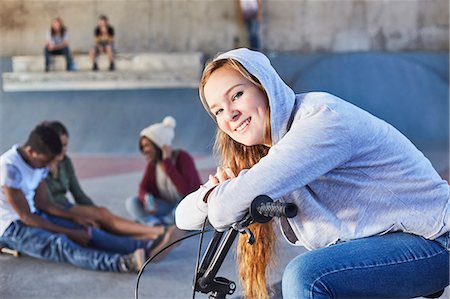 Portrait smiling teenage girl leaning on BMX bicycle at skate park Stock Photo - Premium Royalty-Free, Code: 6113-08698236