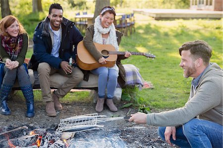 simsearch:6113-08743597,k - Friends playing guitar and cooking fish in grill basket over campfire Stock Photo - Premium Royalty-Free, Code: 6113-08743484