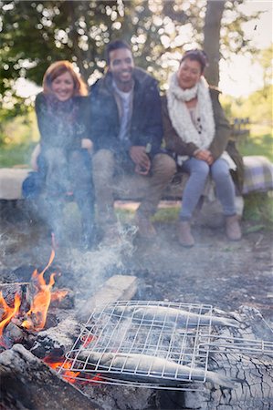 simsearch:6113-08743597,k - Friends watching fish cooking in grill basket on campfire Stock Photo - Premium Royalty-Free, Code: 6113-08743496