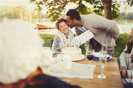 simsearch:6113-08659553,k - Boyfriend kissing girlfriend with birthday gift at lakeside patio table Stock Photo - Premium Royalty-Free, Code: 6113-08743563