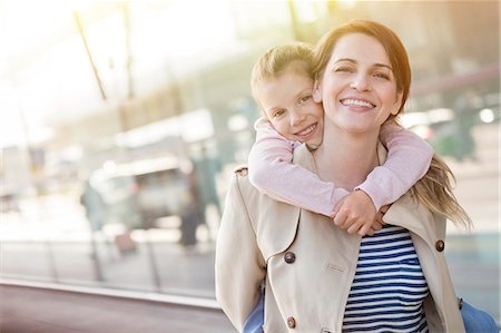 simsearch:6113-06909372,k - Portrait smiling mother piggybacking daughter outside airport Stock Photo - Premium Royalty-Free, Code: 6113-08784162