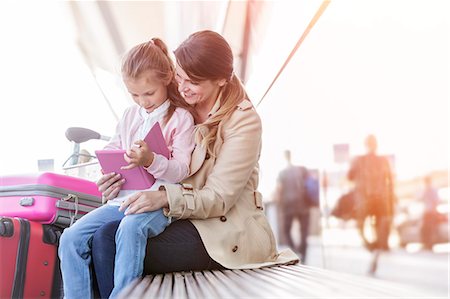 Mother and daughter using digital tablet on bench outside airport Stock Photo - Premium Royalty-Free, Code: 6113-08784177