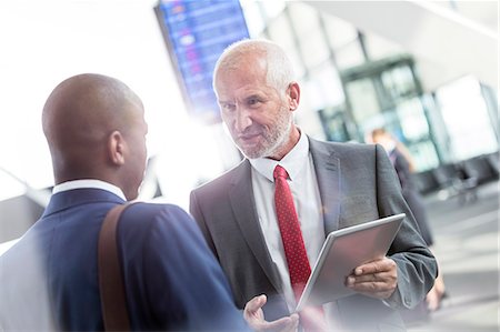 Businessmen talking using digital tablet in airport concourse Stock Photo - Premium Royalty-Free, Code: 6113-08784287