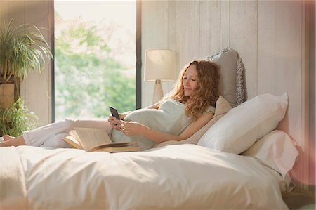 red haired woman - Pregnant woman laying relaxing with book and texting with cell phone in bed Stock Photo - Premium Royalty-Free, Code: 6113-08722007