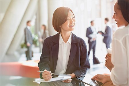 simsearch:614-02985267,k - Smiling businesswomen meeting reviewing paperwork in office lobby Stock Photo - Premium Royalty-Free, Code: 6113-08882427