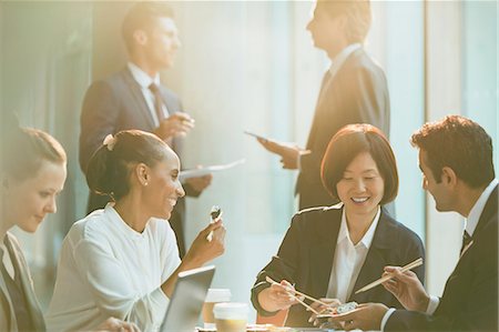 Smiling business people eating lunch with chopsticks in conference room meeting Stock Photo - Premium Royalty-Free, Code: 6113-08882424