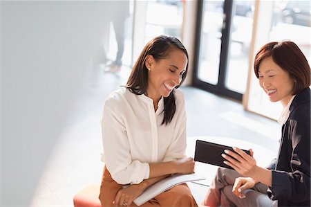 simsearch:614-02985267,k - Smiling businesswomen using digital tablet in office lobby Stock Photo - Premium Royalty-Free, Code: 6113-08882543