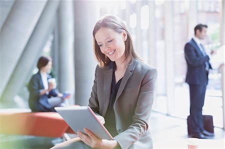 simsearch:6113-07243187,k - Smiling businesswoman using digital tablet in sunny office lobby Stock Photo - Premium Royalty-Free, Code: 6113-08882504