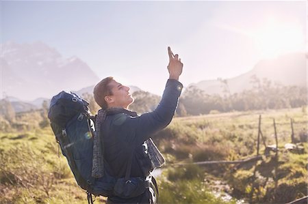 Young man with backpack hiking and using camera phone in sunny, remote field Stock Photo - Premium Royalty-Free, Code: 6113-08882776