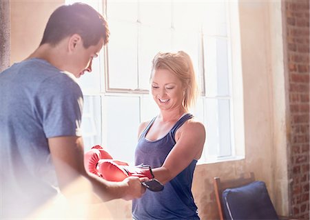 Trainer helping young female boxer putting on boxing gloves in studio Stock Photo - Premium Royalty-Free, Code: 6113-08805532